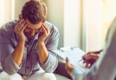 A man sitting with his elbows resting on his knees and his hands holding his head, suggesting he might be feeling stressed or overwhelmed.