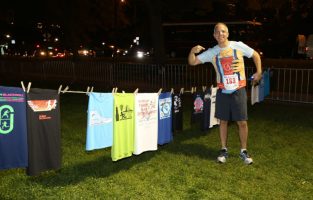 Howard Ankin beside a clothesline full of tshirts, pointing at winning Race Judicata t-shirt design he&#039;s wearing