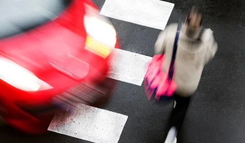 Red car almost hitting a walking pedestrian.