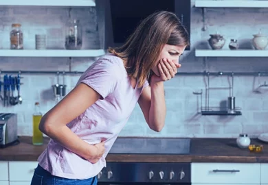 Sick woman about to throw up while standing in the kitchen.