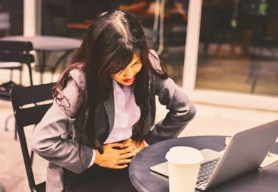 Woman in business suit holding her lower abdomen due to pain.
