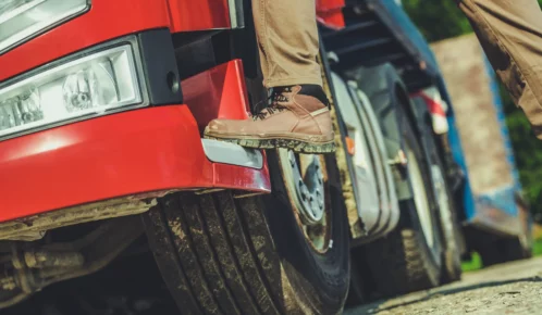 Truck driver wearing ankle boots stepping up on a red truck.