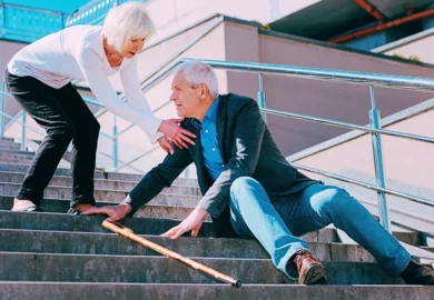 Elder man sitting on a step of the chair after he slipped with an elder woman helping him.