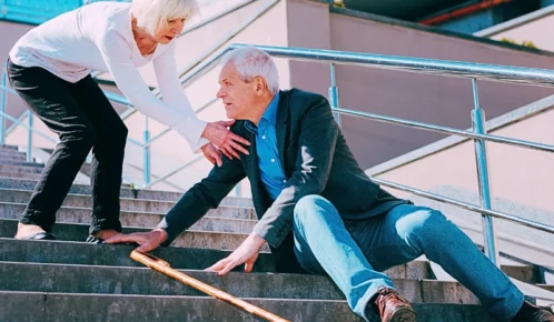 Elder man sitting on a step of the chair after he slipped with an elder woman helping him.