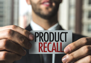 Man in suit holding a piece of paper with Product Recall printed in black and red.