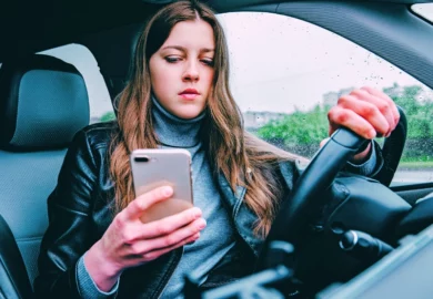 Young woman using mobile phone while driving car on bad weather condition. Driving While Distracted
