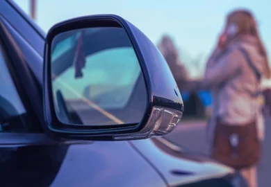 Woman on the phone in front of a black car. Injured in an Uber or Lyft