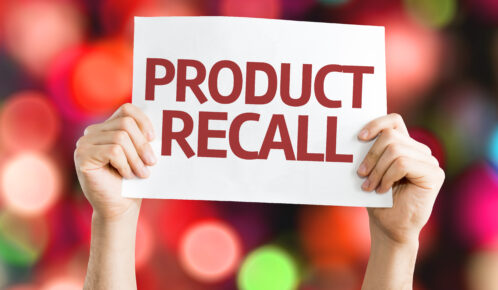 Hands holding product recall printed on a white paper with blurry lights in the background.