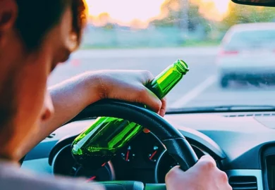 Drunk young man driving a car with a bottle of beer.
