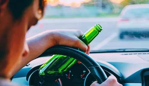 Drunk young man driving a car with a bottle of beer.