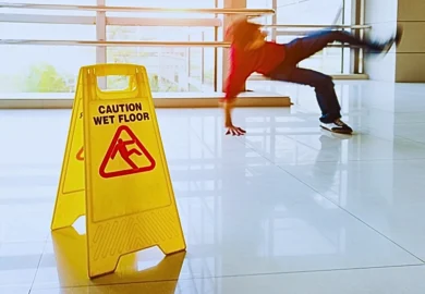 Man slips falling on wet floor next to the wet floor caution sign. Building Code Violations Can Lead to Slip and Fall Accidents