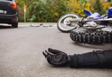 Motorcycle accident scene showing a rider's gloved hand on the road near a fallen bike.