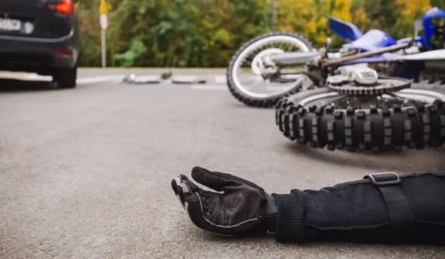 Motorcycle accident scene showing a rider's gloved hand on the road near a fallen bike.