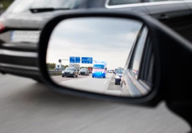 Ambulance with flashing lights seen in a car’s side mirror on a highway.