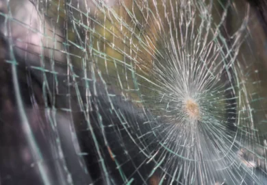 Close-up image of a shattered glass surface with a central impact point and radiating cracks.