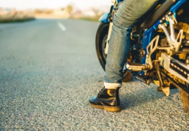 A person wearing jeans and black boots sits on a blue motorcycle parked on an empty road.