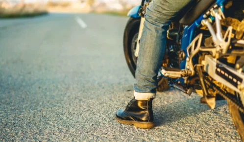 A person wearing jeans and black boots sits on a blue motorcycle parked on an empty road.
