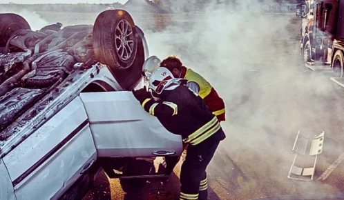 On the car crash traffic accident scene: rescue team of firefighters pull victim out the roll over vehicle.