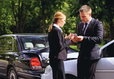 Two people in business attire standing near two cars that have been involved in a minor collision. Handle a Lowball Settlement Offer