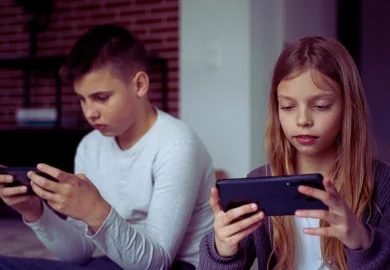 two children sitting side by side, each holding a handheld device, likely smartphones or gaming consoles.