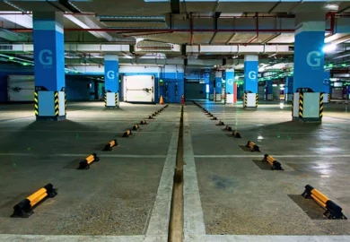 an empty underground parking garage with clearly marked parking spaces separated by wheel stops. Parking Garage Injury Claims