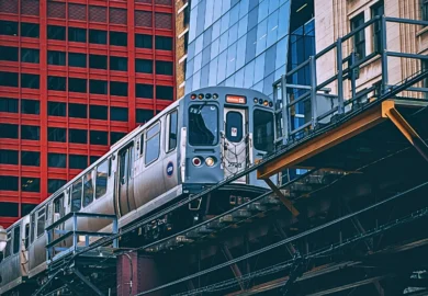 a silver elevated subway train traveling on steel tracks above a city street in Chicago.