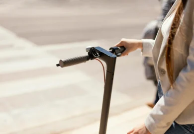 Person riding electric scooter outdoors holding handlebar close-up.