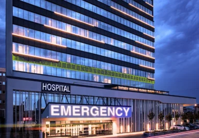 Modern hospital building with a glowing blue emergency entrance.