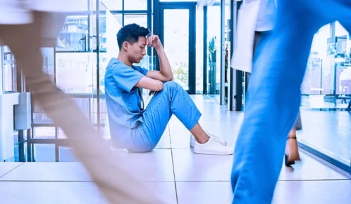 Exhausted healthcare worker sitting on a busy hospital floor. Hospital Understaffing