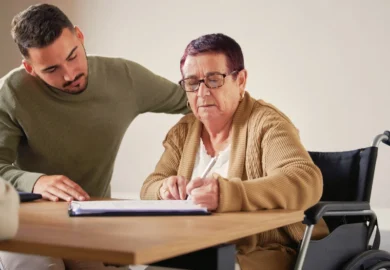 A man assists an elderly woman signing some documents.