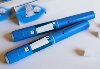 Two blue insulin pens lying on a white surface.