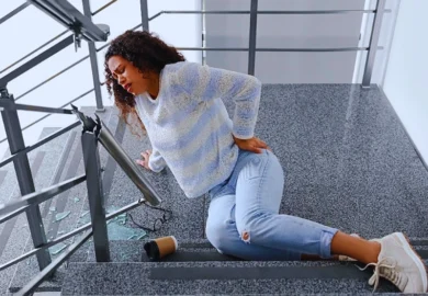 Woman clutching her back after falling down stone stairs. Injured Because a Staircase Handrail Broke