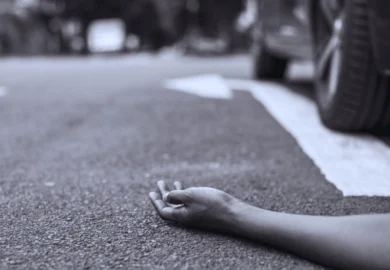 A person's hand lying on asphalt near a car.