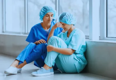 Healthcare worker comforting her exhausted colleague on hospital floor. alarm fatigue