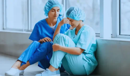 Healthcare worker comforting her exhausted colleague on hospital floor. alarm fatigue