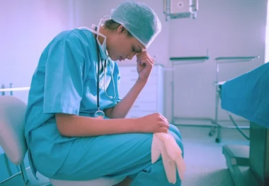An exhausted surgeon sits in an operating room looking stressed.