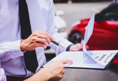 Two people review an insurance policy clipboard near a car. insurance companies ask for recorded statements