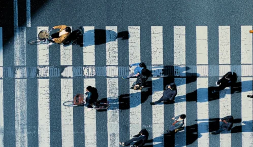 Aerial view of pedestrians and cyclists crossing a striped crosswalk.