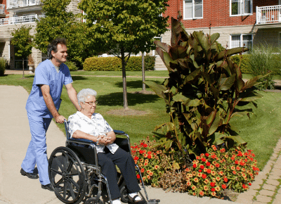 A male nurse wheels an elderly woman through a neighborhood.